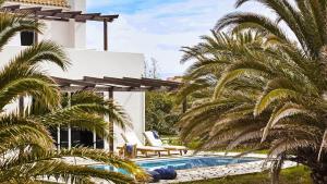 a pool with palm trees in front of a house at Kymata Bohemian Villas in Lixouri