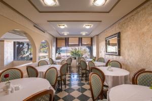 un restaurante con mesas y sillas blancas y ventanas en Jolly Hotel, en Igoumenitsa