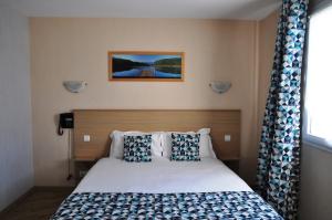 Schlafzimmer mit einem Bett mit blauen und weißen Kissen in der Unterkunft Brit Hotel Azur in Saint-André-de-la-Marche