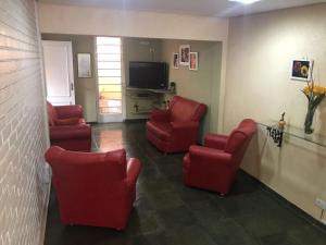 a waiting room with red chairs and a tv at Pousada Hostel Universitário in Londrina