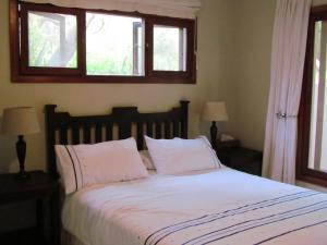 a bedroom with a bed with white sheets and two windows at Nkumbe Bush Retreat Family Home in Ponta Malongane