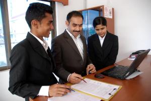 three men in suits standing around a desk with a laptop at The Bodhgaya Hotel School in Bodh Gaya