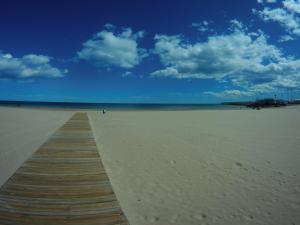 a wooden boardwalk on a beach with a blue sky at Hotel Albatros in Gandía