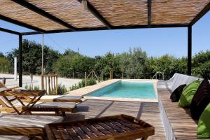 a pool with a wooden deck with chairs and a table at Monte Belo Romão in Olhão