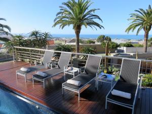 a deck with chairs and a swimming pool with palm trees at Island Way Villa in Port Elizabeth