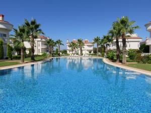 a large swimming pool with palm trees and buildings at Sadev Turizm Belek Family Villas in Belek