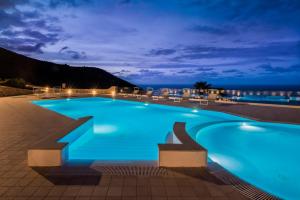 een blauw zwembad 's nachts met de oceaan op de achtergrond bij Hotel Parco Degli Aromi Resort & SPA in Valderice
