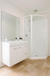 a white bathroom with a sink and a shower at Te Whau Bach Apartments in Te Whau Bay