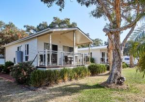 a white house with a porch and a tree at Budgewoi Holiday Park in Budgewoi