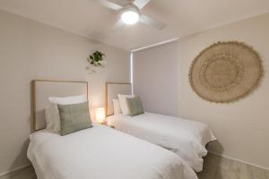 two beds in a white room with a ceiling fan at Number 72 Kalbarri Riverview Apartments in Kalbarri