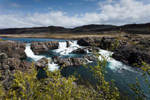 a river with rocks and waterfalls in a field at Bifröst Apartments in Bifrost +13 photos