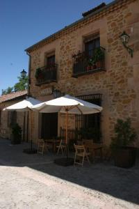 duas mesas e guarda-chuvas em frente a um edifício em La Posada de Don Mariano em Pedraza-Segovia