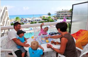 una familia jugando un juego de mesa en una mesa en un balcón en Résidence Goélia Royal Cap en Villeneuve-Loubet