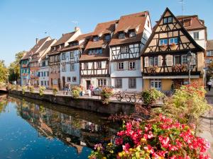 un groupe de bâtiments à côté d'une rivière fleurie dans l'établissement Gîtes Schwendi - Quartier Petite Venise, à Colmar