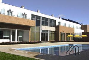 a building with a pool in front of a building with umbrellas at Hotel A Esteva in Castro Verde