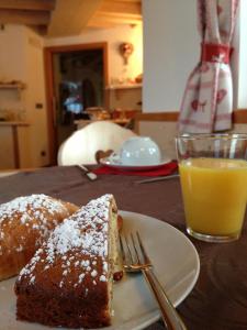 un trozo de pastel en un plato junto a un vaso de zumo de naranja en Affittacamere Famiglia Ceschini, en Tesero