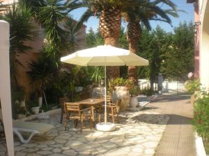 una mesa y sillas con sombrilla y palmeras en Acharavi Afrodite Apartments, en Acharavi