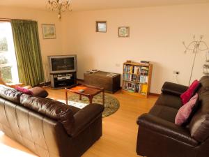Sala de estar con 2 sofás de cuero y TV en Atlantic Bay Cottage, en Clachan