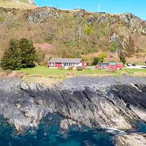 a house on the side of a mountain next to the water at Atlantic Bay Cottage in Clachan