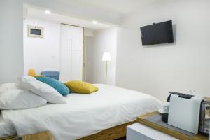 een witte slaapkamer met een bed met kussens en een televisie bij The Grape House in Akko