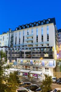 un grande edificio bianco con auto parcheggiate in un parcheggio di Hôtel Astrid a Lourdes