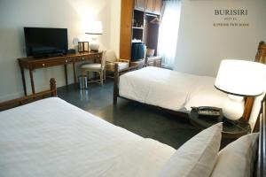 a room with two beds and a desk with a television at Buri Siri Boutique Hotel in Chiang Mai