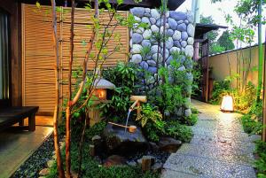 a garden with a stone wall and a small shrine at Oiwakeya Ryokan in Matsumoto