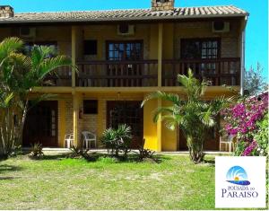 una casa amarilla con palmeras delante en Pousada do Paraiso, en Barra de Ibiraquera