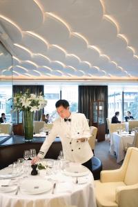 a man in a white suit standing at a table in a restaurant at Mandarin Oriental Hong Kong in Hong Kong