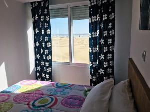 a bedroom with a bed and a window with the beach at Apartamentos Calypso in Punta Umbría