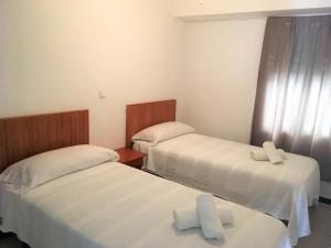 two beds in a small room with white sheets at Apartamentos Calypso in Punta Umbría