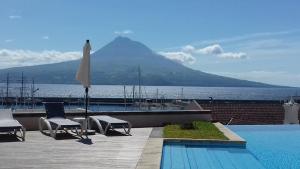 a pool with an umbrella and chairs and a mountain at Azoris Faial Garden – Resort Hotel in Horta