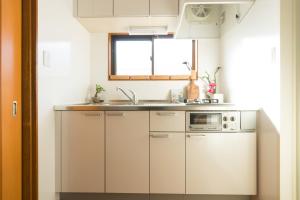 cocina con armarios blancos, fregadero y ventana en K&K Apartment Kita-Akabane #301 en Tokio