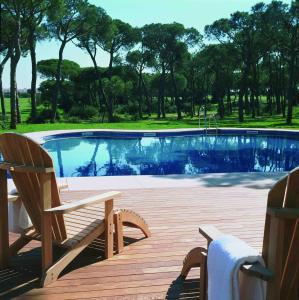 - une piscine avec deux chaises à côté d'une terrasse en bois dans l'établissement Hotel Nuevo Portil Golf, à El Rompido