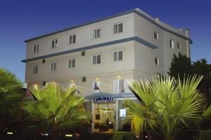 a large white building with palm trees in front of it at Hotel Residencial Colibri in Costa da Caparica