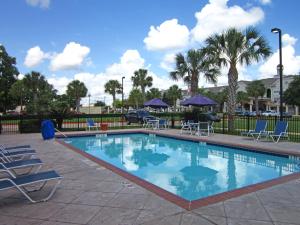 a swimming pool with chairs and tables and trees at LoneStar Suites in Webster