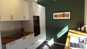 a kitchen with white cabinets and a green wall at La petite maison in Aywaille