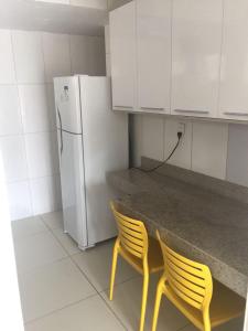 cocina con 2 sillas amarillas y nevera blanca en Apartamento San Lorenzo, en Maceió