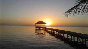 ein Pier mit einem Pavillon auf dem Wasser bei Sonnenuntergang in der Unterkunft Cocotal Inn and Cabanas in San Pedro