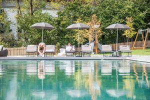 Ein Mann und ein Hund sitzen auf Stühlen neben einem Swimmingpool. in der Unterkunft Hotel Kronblick in Kiens