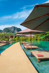 a pool with lounge chairs and umbrellas at PP Charlie Beach Resort- SHA Plus in Phi Phi Don