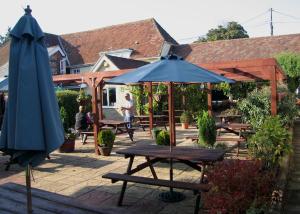 um pátio com uma mesa, um guarda-chuva e bancos em The Pelican Inn em Stapleford