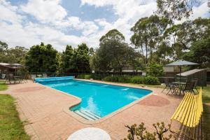una piscina con un patio de ladrillo y sillas amarillas en Phillip Island Park Lane Holiday Park, en Cowes