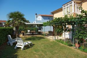 a yard with two white chairs in the grass at Apartments & Rooms BARBARA in Umag