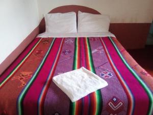 a bed with a multicolored blanket with a white towel on it at Luquina homestay in Puno