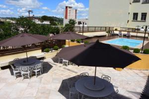 an outdoor patio with tables and umbrellas and a pool at Hotel Cosini in São Sebastião do Paraíso