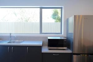 a kitchen with a microwave and a sink and a refrigerator at Stopforths Motel in Hokitika
