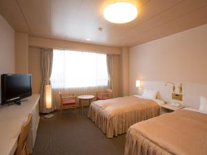 a hotel room with two beds and a television at Itoen Hotel Kusatsu in Kusatsu