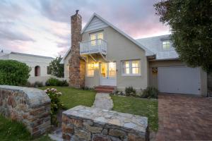 a white house with a porch and a brick wall at Stone Chimney Cottage in Hermanus