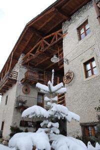 a building covered in snow with a tree in front at Agriturismo Barba Gust in Cesana Torinese